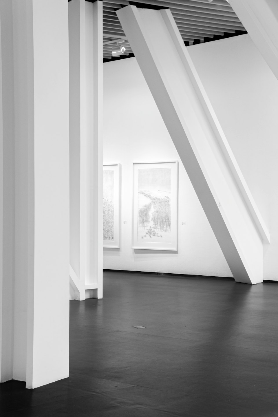 Zwei Kunstwerke hängen an einer weißen Wand in einer minimalistischen Galerie.